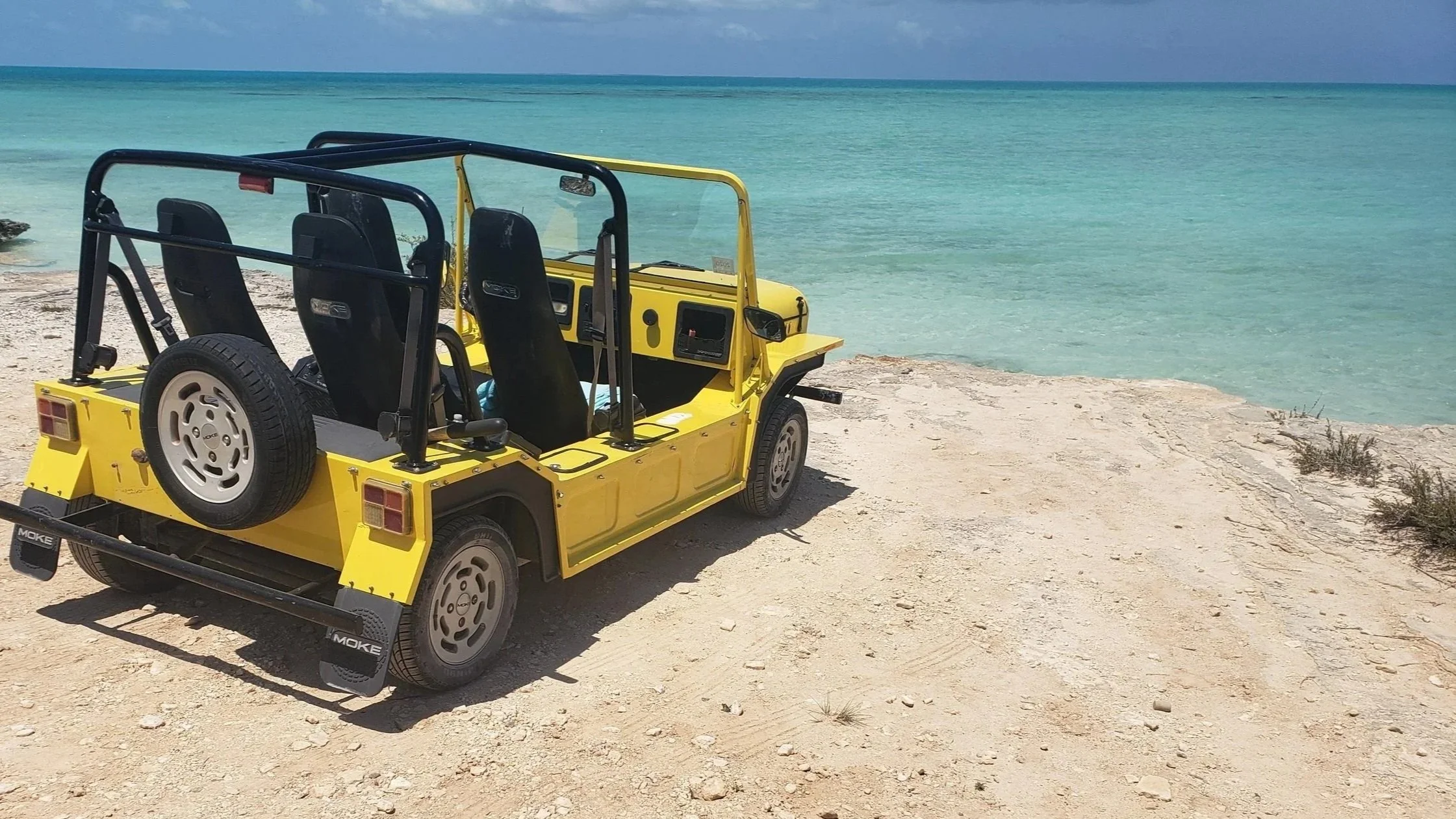 Yellow Moke cruising on a scenic coastal road with ocean views